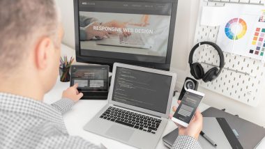 Web designer, programmer working with responsive web template. Multiple devices on desk.